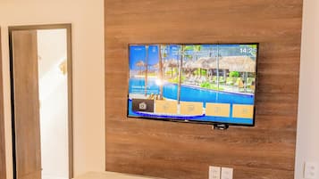 Habitación de hotel moderna con un televisor de pantalla plana grande montado en un panel de madera, un escritorio blanco con una silla y un espejo grande en la pared.
