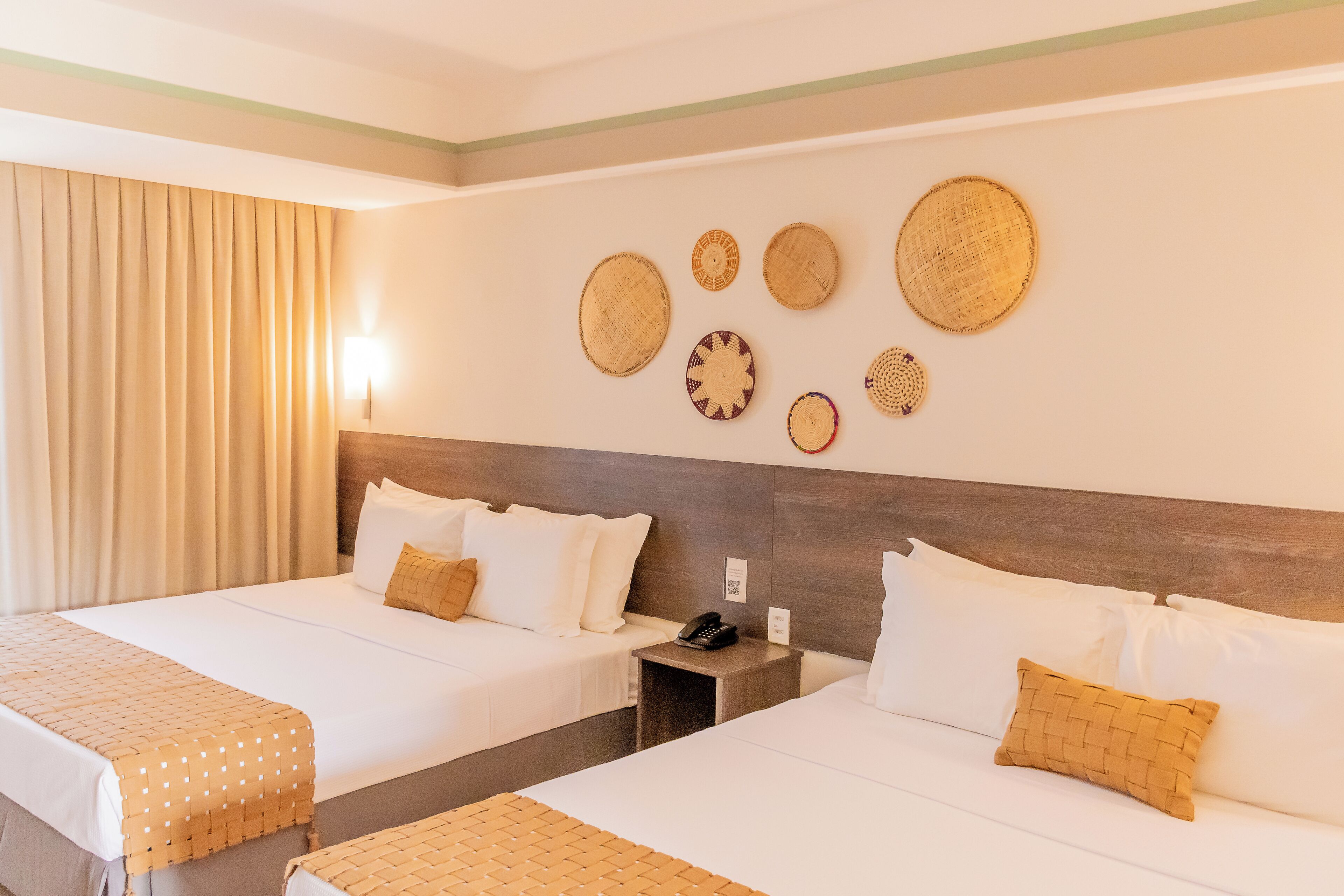 Ein Hotelzimmer mit zwei Betten, einem Nachttisch mit Telefon und Wanddekoration, darunter gewebte Körbe.