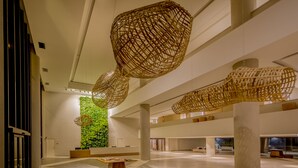 A spacious lobby with high ceilings, large columns, and hanging wicker chandeliers.