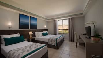 A hotel room with two beds, a desk, a TV, and a window with a view.