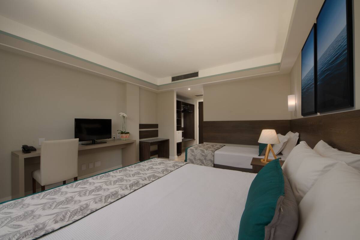 A hotel room with a large bed, a desk with a TV, a chair, a small table with a lamp, and a wardrobe.