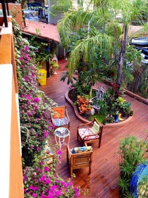 Una terrassa de fusta amb mobiliari exterior, envoltada de vegetació exuberante i plantes florejants.