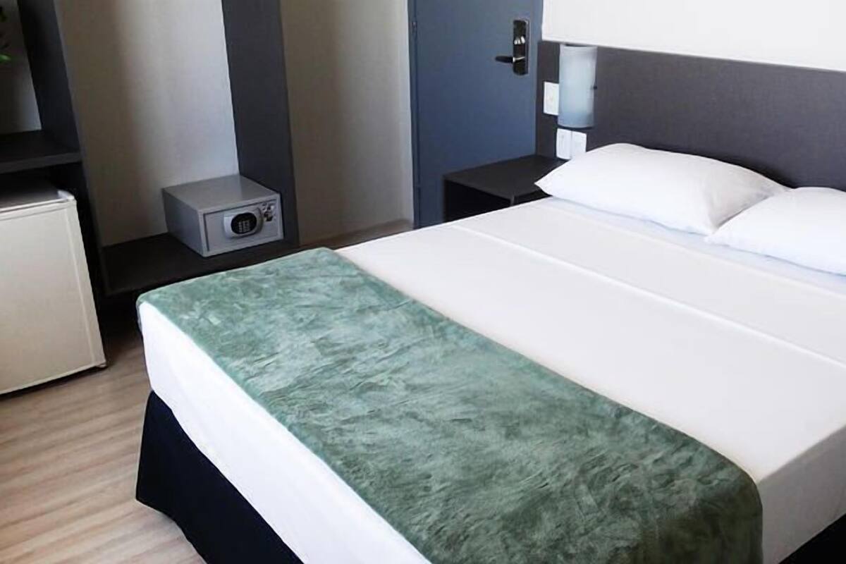 Une chambre d’hôtel avec un lit, une table de chevet, une petite armoire et une porte.