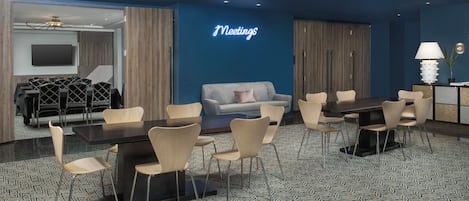 A modern meeting room with a blue accent wall, a large table with chairs, a sofa, and a television.