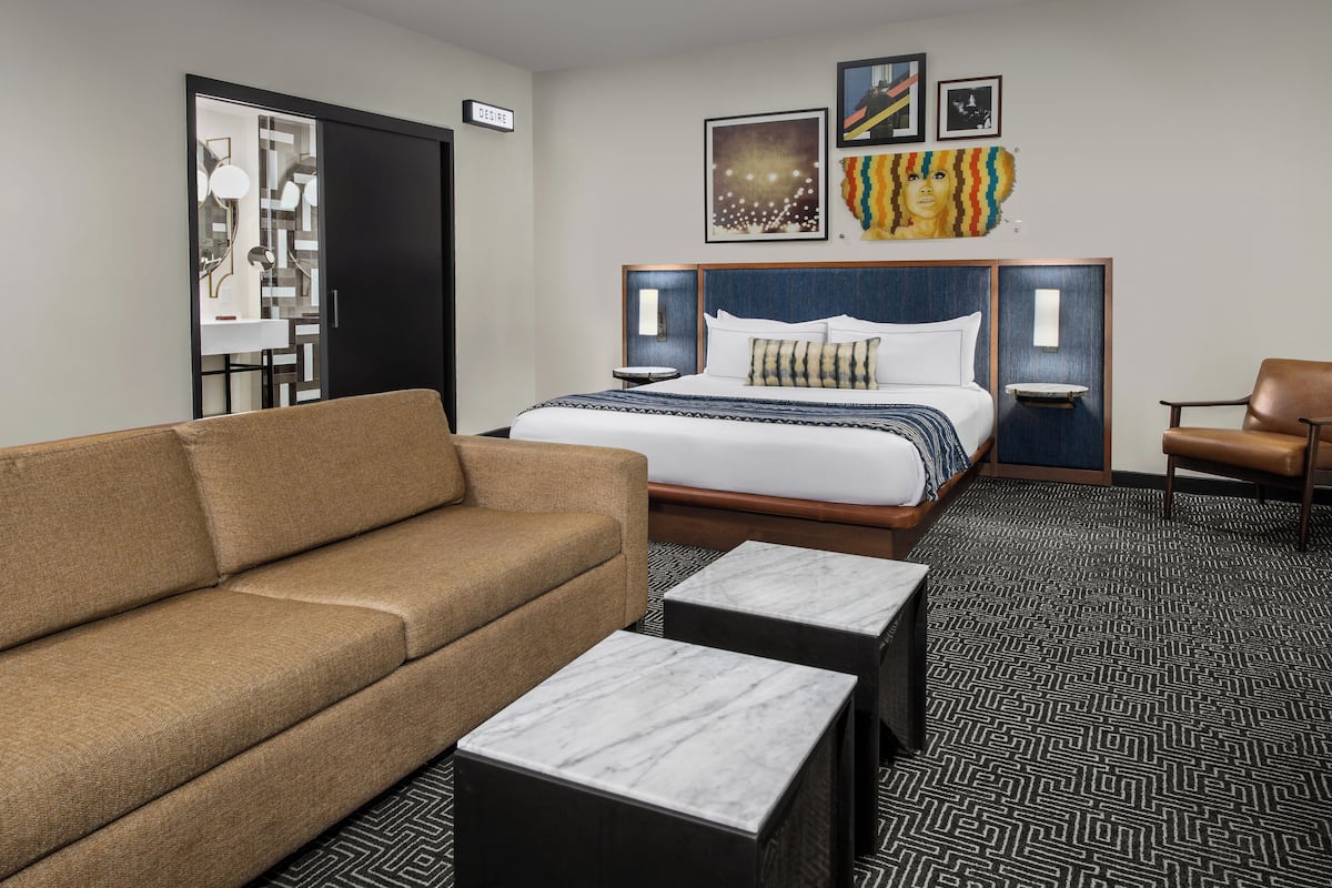 A hotel room with a bed, a sofa, two side tables, and a chair.