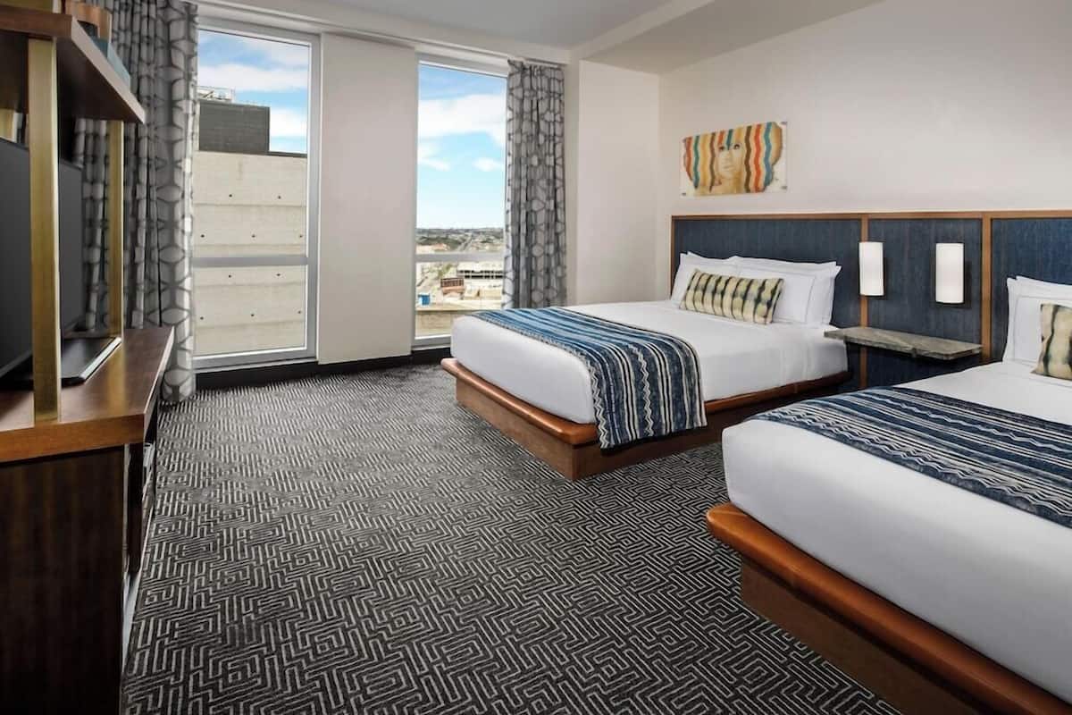 A hotel room with two beds, a large window with a view, and a television on a wooden stand.
