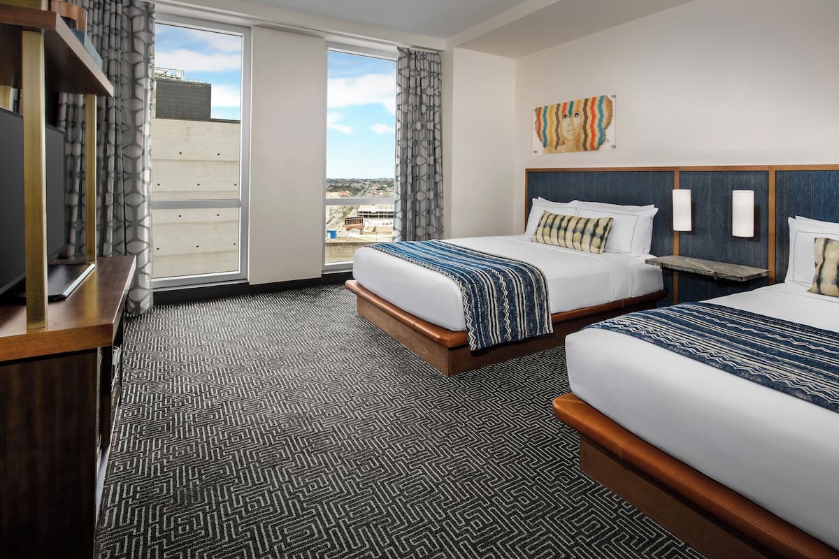 A hotel room with two beds, a large window with a view, and a television on a wooden stand.