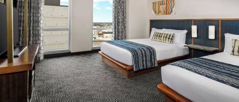 A hotel room with two beds, a large window with a view, and a television on a wooden stand.