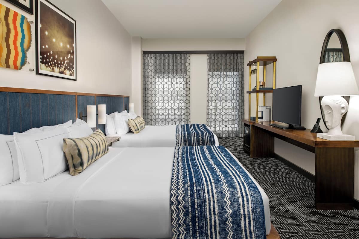 A hotel room with two beds, a desk with a computer, a TV, and a lamp.