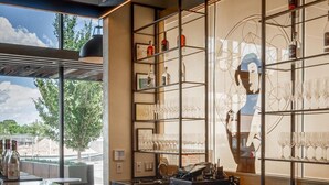 A modern bar area with a reflective marble countertop, shelves with glasses and bottles, and a large window offering a view of the outdoors. - Hotel Chaco (Albuquerque)