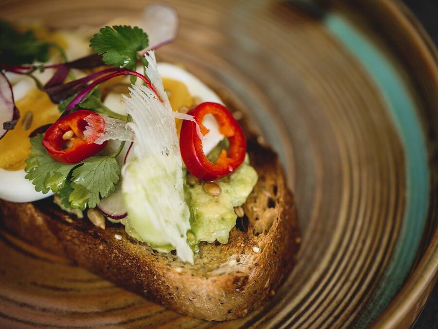 Een sneetje toast met avocado, rode peper en een gekookt ei, geserveerd op een keramieken bord.