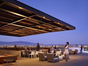 Un espace extérieur aménagé avec des sièges, offrant une vue sur le paysage urbain et les montagnes.