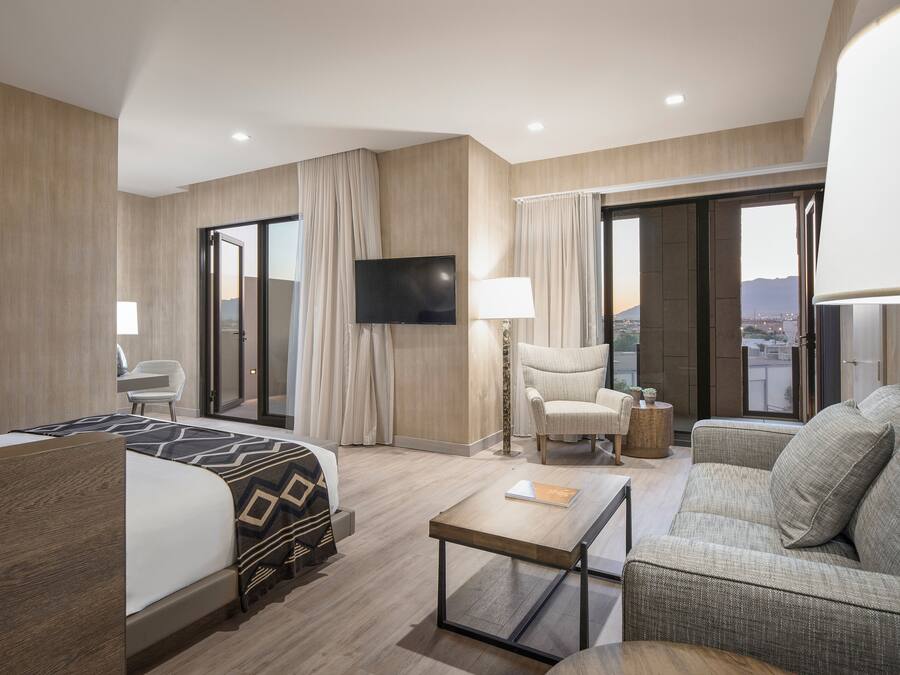 A hotel room with a bed, a sofa, a TV, and a view of the city.
