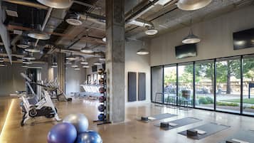 Une salle de sport spacieuse, équipée de matériel d’exercice, dotée de grandes fenêtres et d’un plafond en béton.