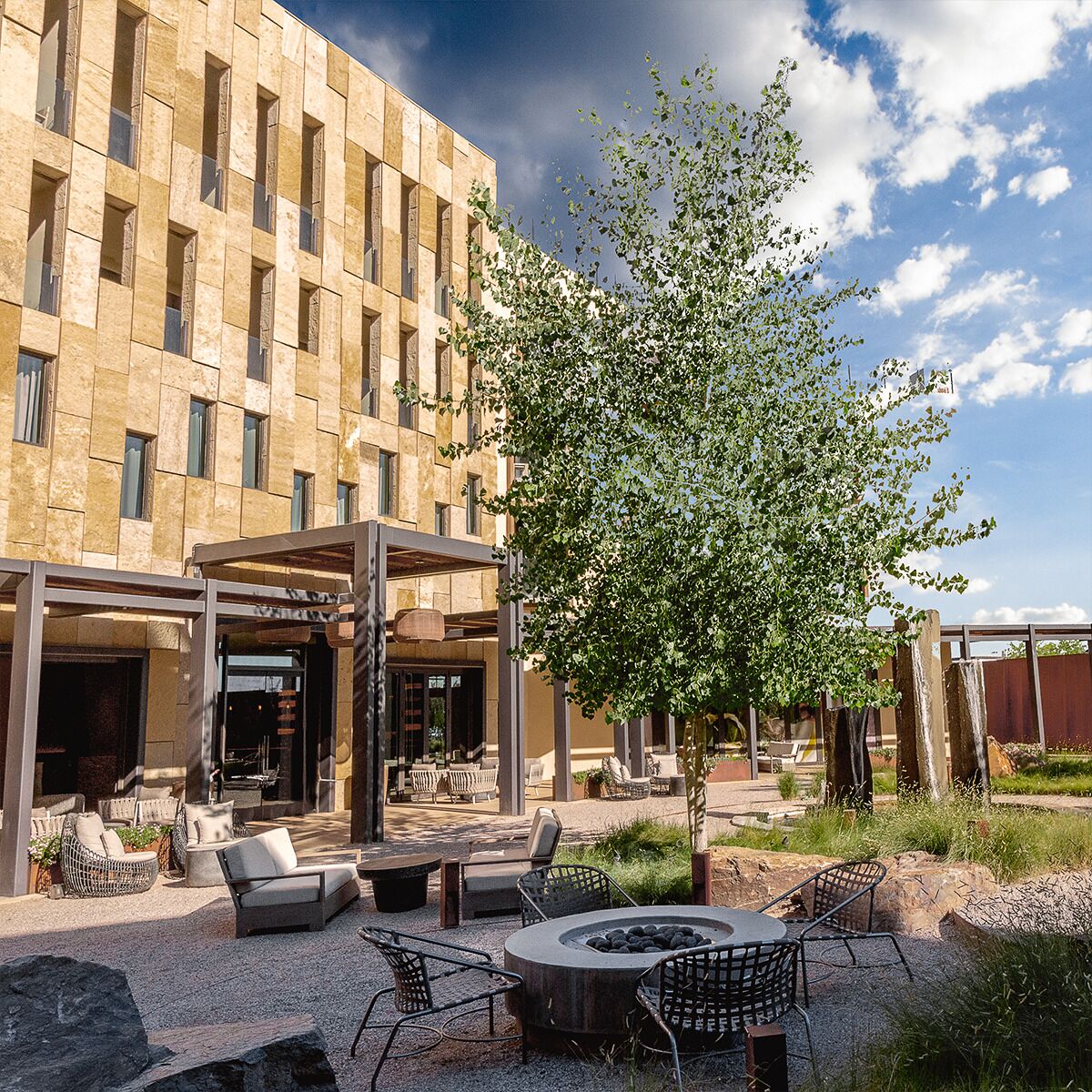 Un bâtiment moderne doté d’une cour intérieure aménagée avec des espaces de détente en plein air, un foyer et un arbre.