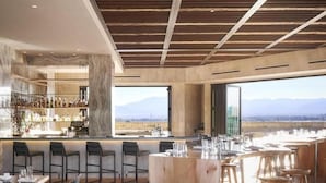 A modern restaurant with a bar area, wooden ceiling beams, and a view of the mountains. - Hotel Chaco (Albuquerque)