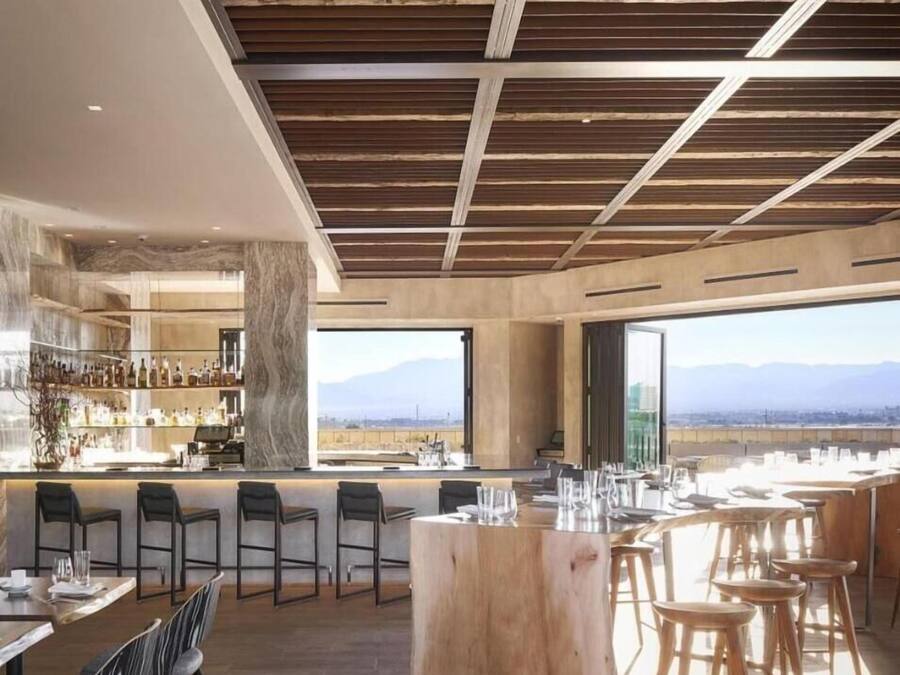 Un restaurant moderne doté d’un bar, de poutres apparentes en bois au plafond et offrant une vue sur les montagnes.