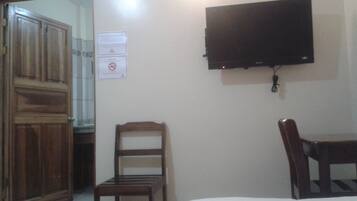 Una habitación con un armario de madera, una silla de madera, una cama y un televisor montado.