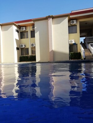 Un edificio con varias unidades de aire acondicionado, una piscina con reflejos claros y una escalera que conduce a un nivel superior.