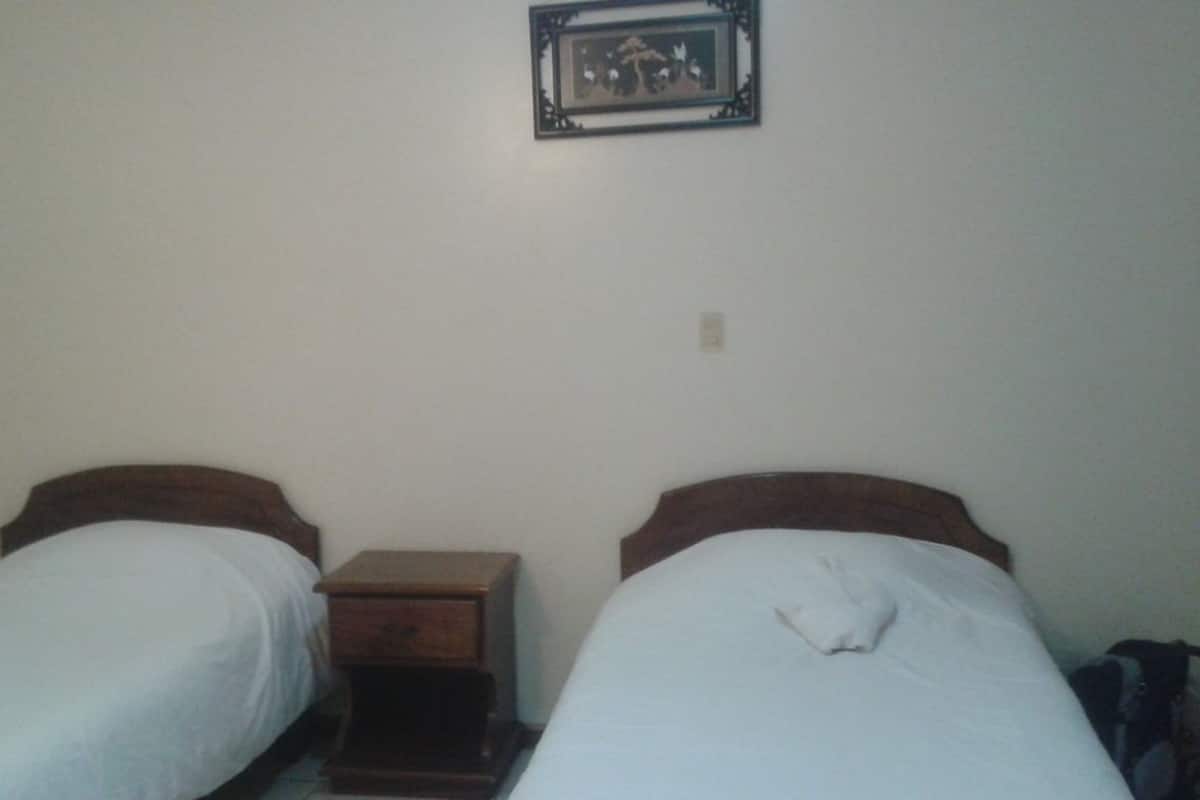 A small, simple room with two single beds, a small wooden nightstand, and a framed picture on the wall.