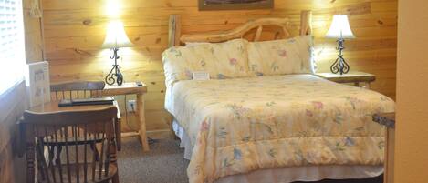 A wooden room with a bed, two bedside tables, a chair, and a painting on the wall.