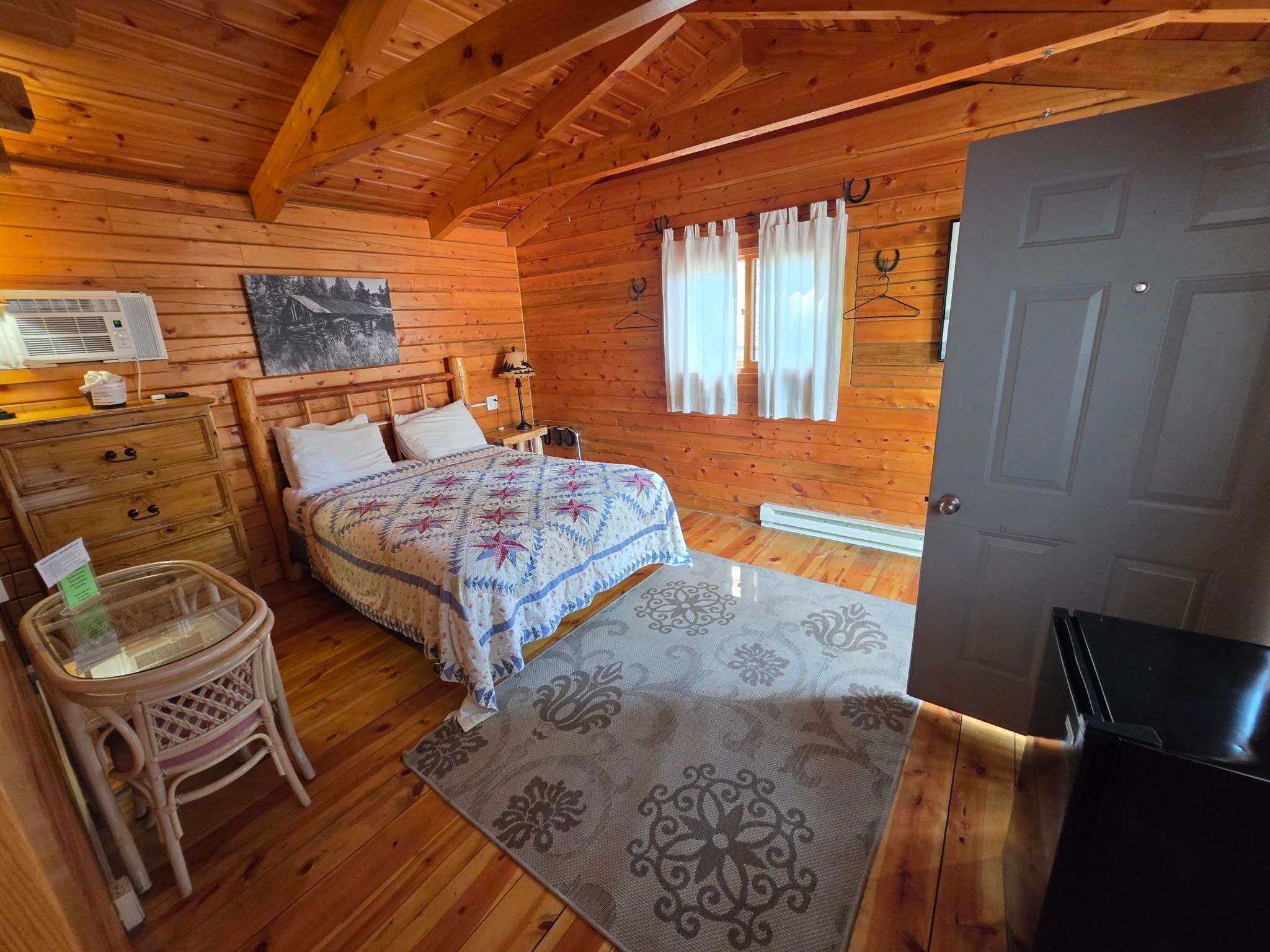 A wooden cabin bedroom with a bed, dresser, and a small table.