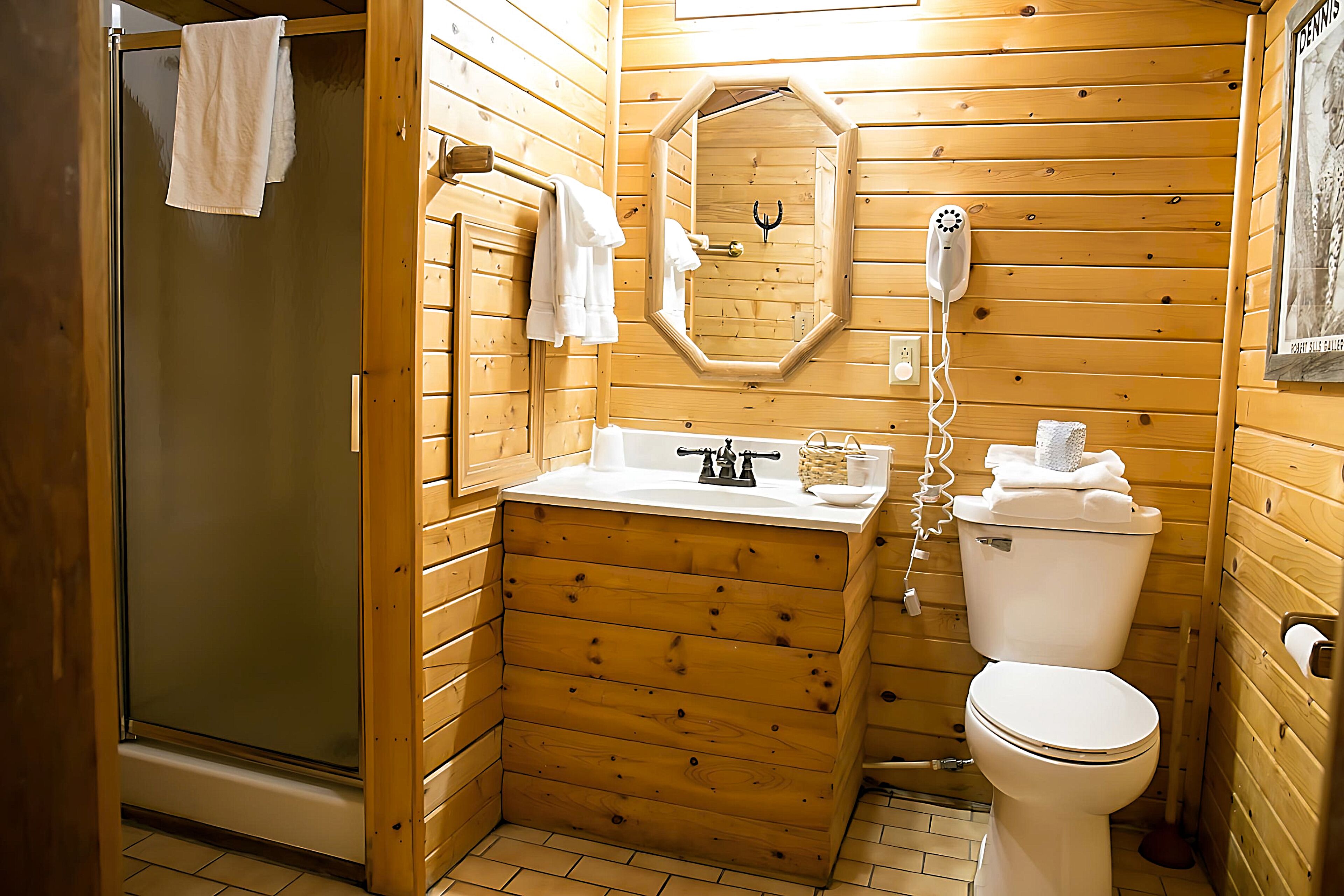 A wooden cabin bathroom with a glass shower enclosure, a wooden vanity with a sink and mirror, and a toilet.