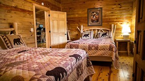 Um quarto estilo cabana de madeira com duas camas, uma porta de madeira, uma moldura com imagem na parede e uma pequena mesa com abajur.
