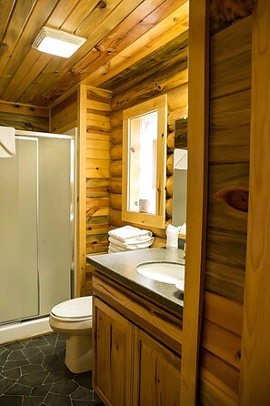 A wooden cabin-style bathroom with a toilet, sink, and mirror.