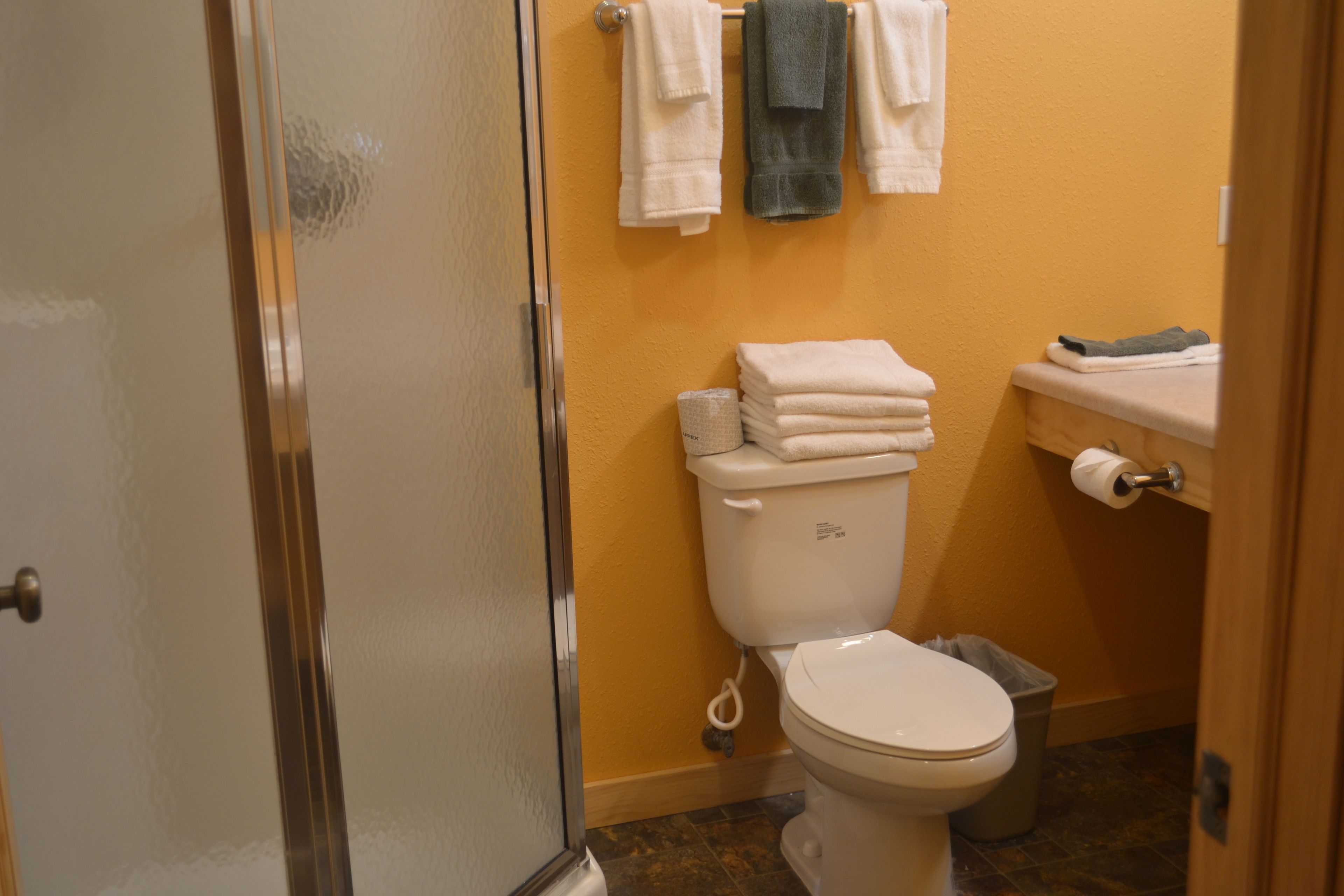 Ein Badezimmer mit Toilette, einem Stapel weißer Handtücher und einem Mülleimer.