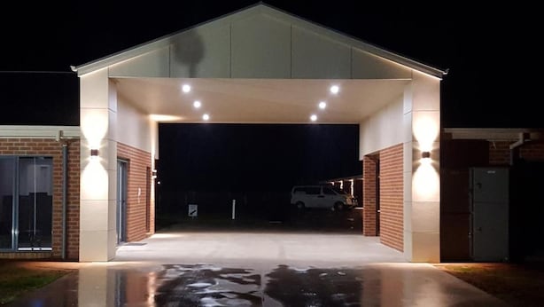 A covered garage entrance with a wet driveway, a white car parked inside, and a brick building on the left. - Euston Motel (Euston)