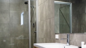 A modern bathroom with a glass-enclosed shower, a wooden vanity with a white sink, and a large mirror above the vanity. - Euston Motel (Euston)