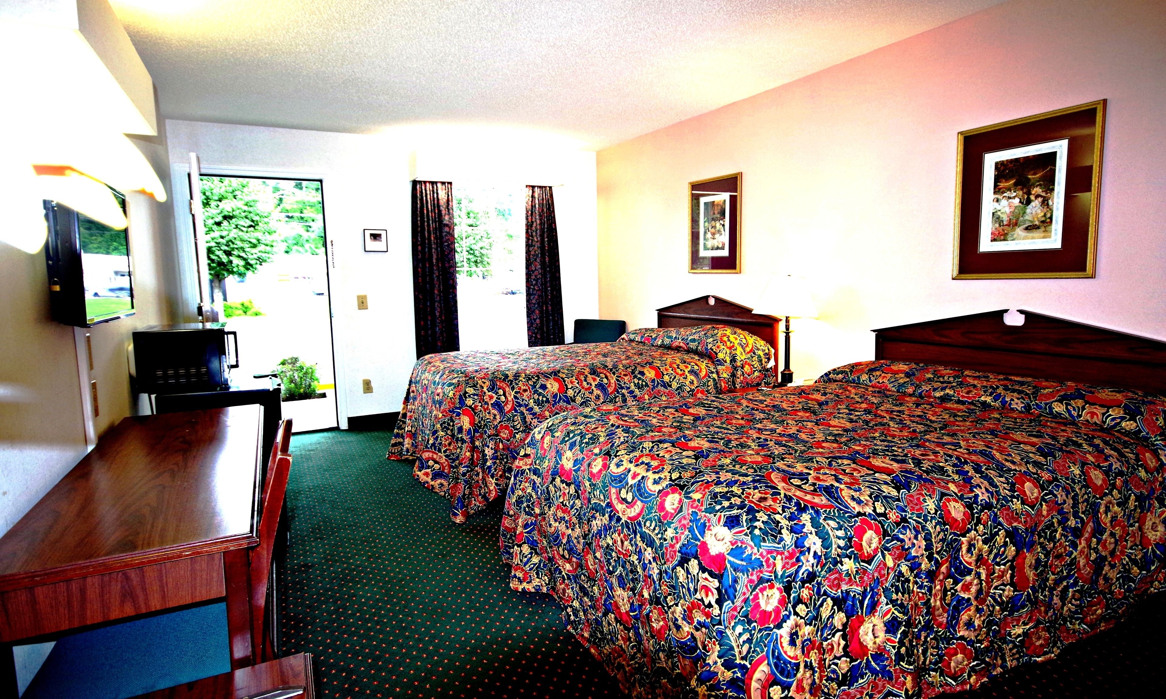 A hotel room with a large bed, a desk, a television, and a door leading to a balcony.