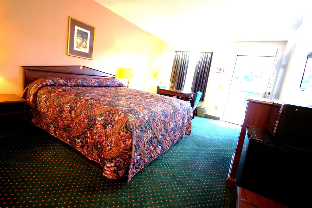 A hotel room with a bed, two bedside tables, a lamp, a chair, a desk, and a door.