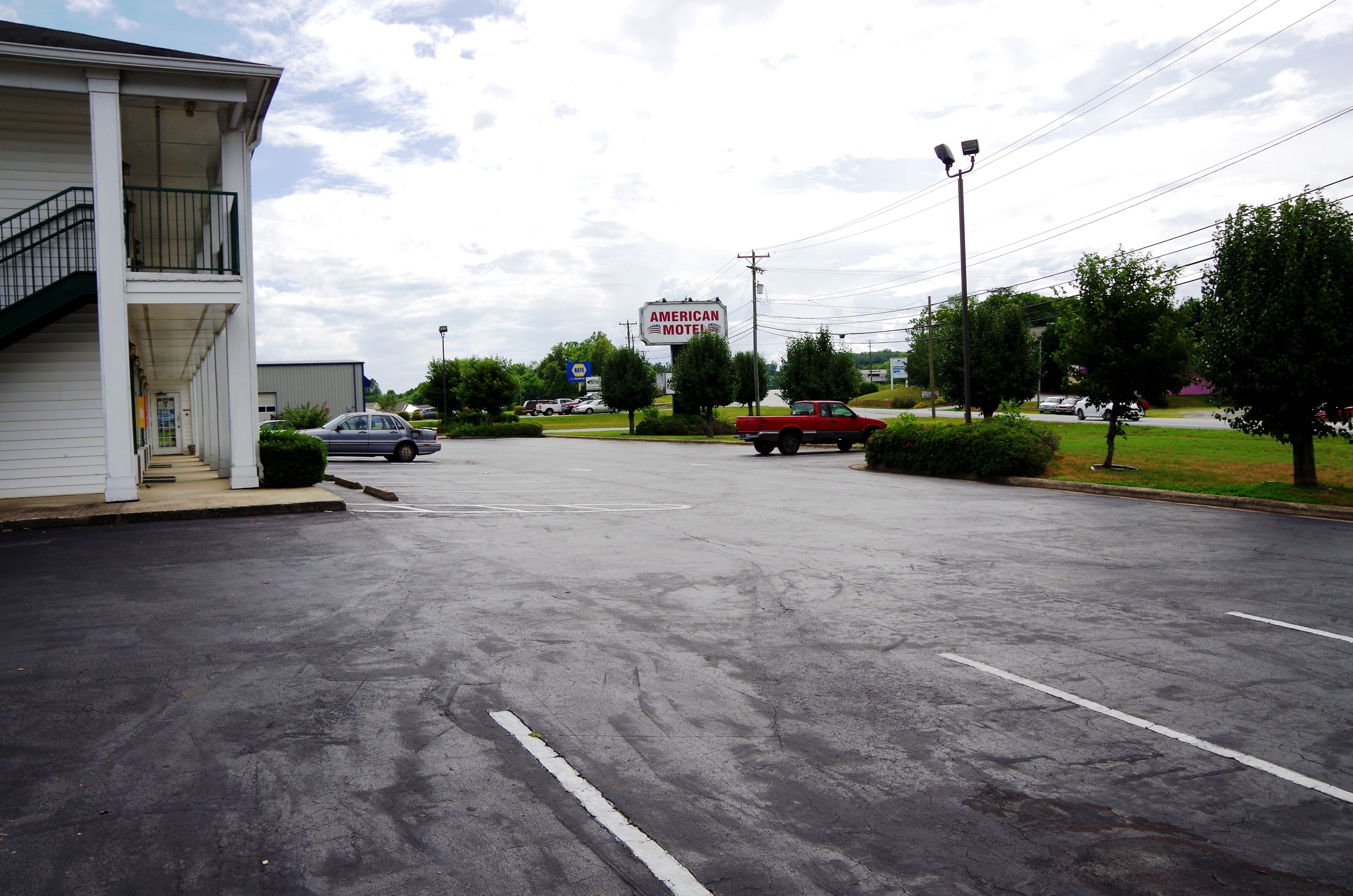 Un motel con zona de estacionamiento techada, un letrero y una camioneta roja estacionada cerca.