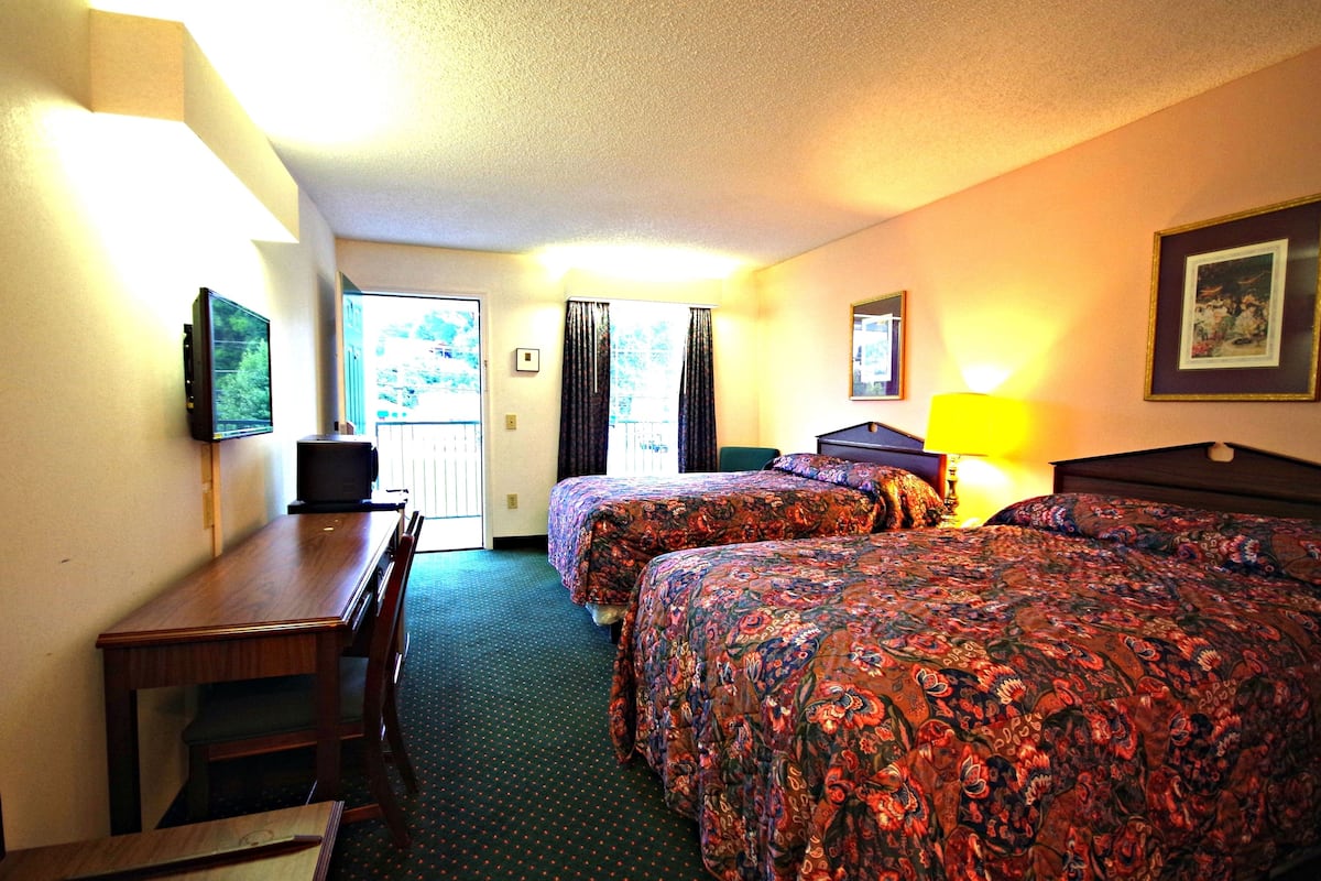 A hotel room with two beds, a desk, a television, and a window with curtains.