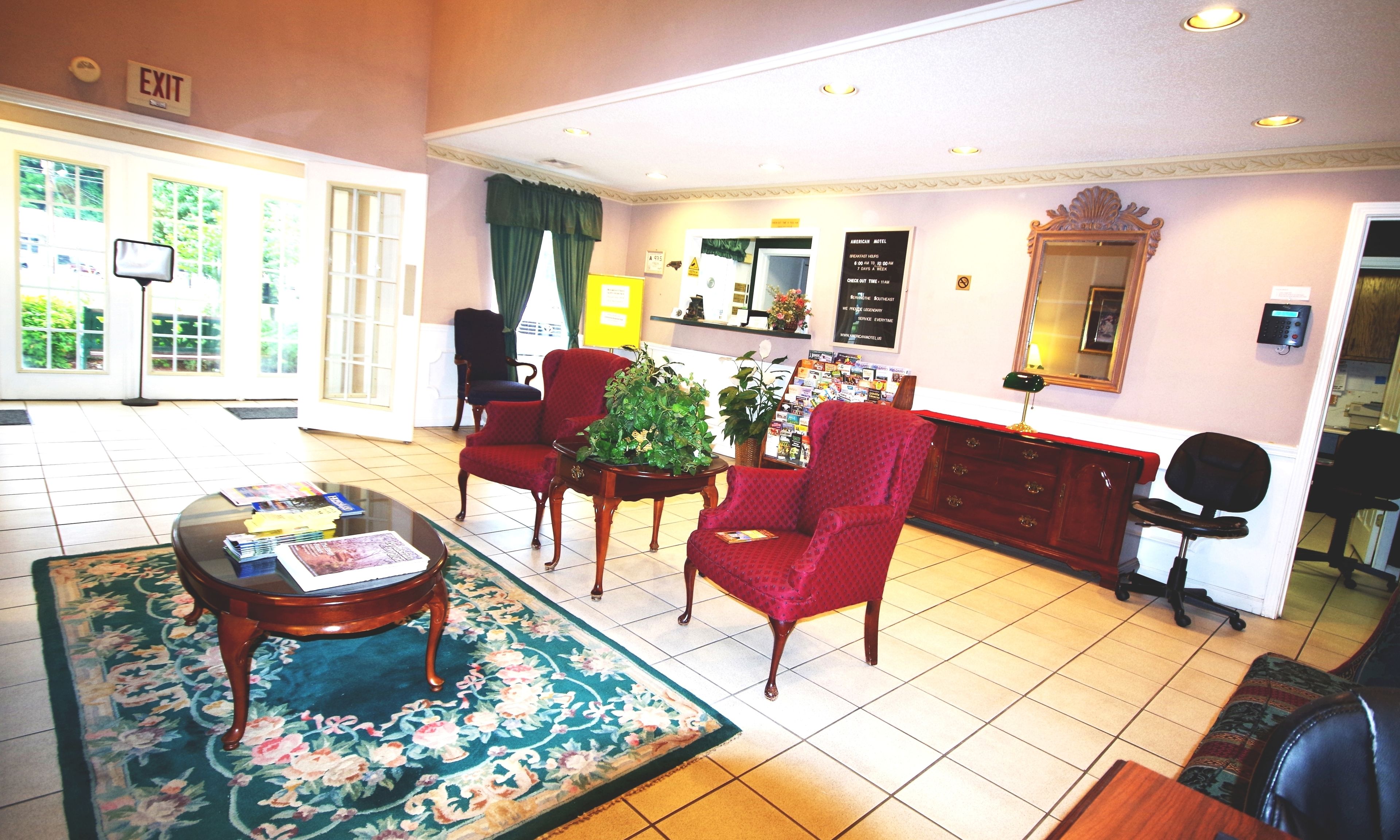 A lobby with a reception desk, red armchairs, a coffee table, and a floral rug.