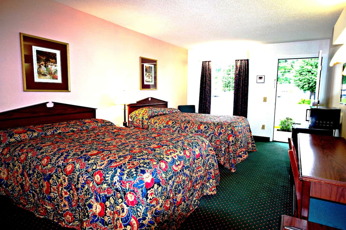 A hotel room with a large bed, two bedside tables, a desk with a chair, a television, and a door leading to a balcony.