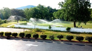 A golf course with multiple water fountains, a white fence, and a road with a directional arrow. - American Motel (Lenoir)