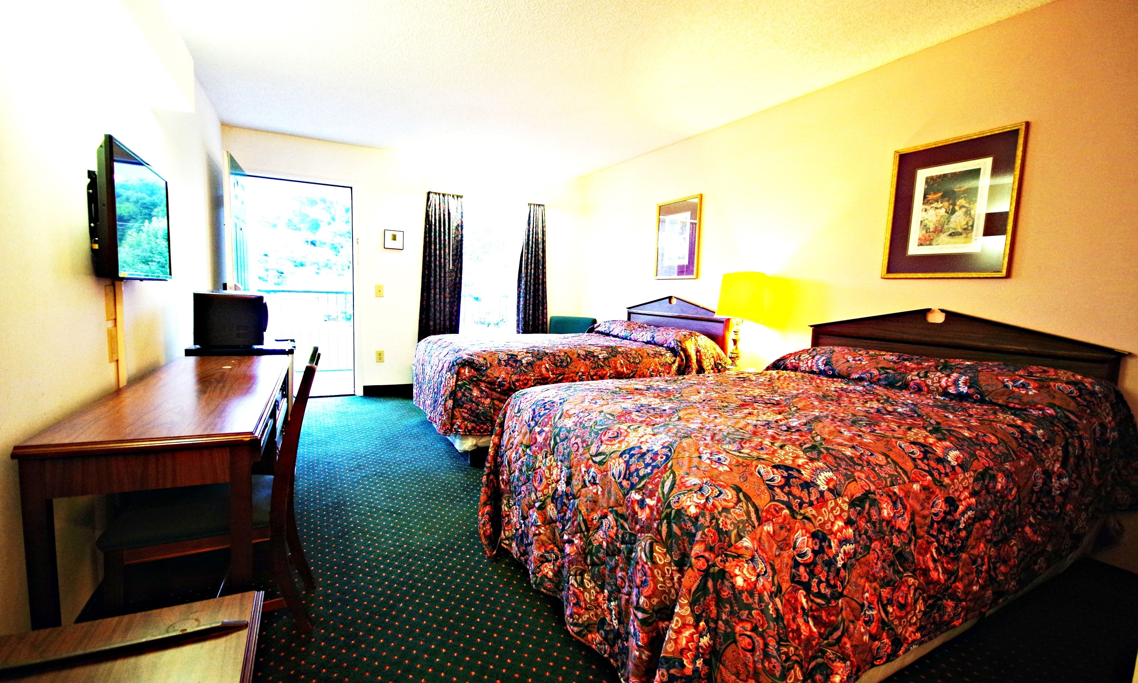 A hotel room with two beds, a desk, a chair, a TV, and a window with curtains.