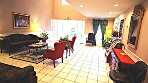 A hotel living room with a sofa, chairs, a coffee table, and a red table with a mirror. - American Motel (Lenoir)