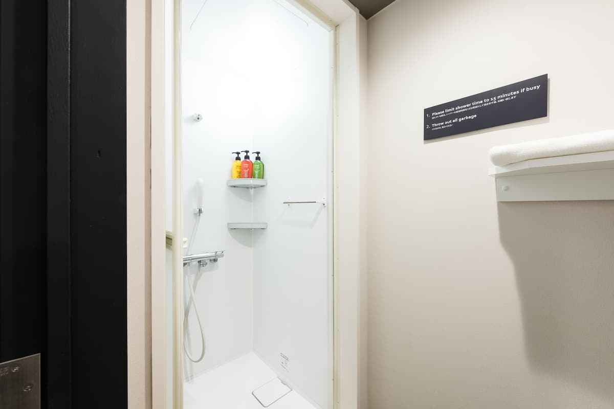 Casa de banho com chuveiro branco, prateleira com artigos de higiene e sinal com instruções.