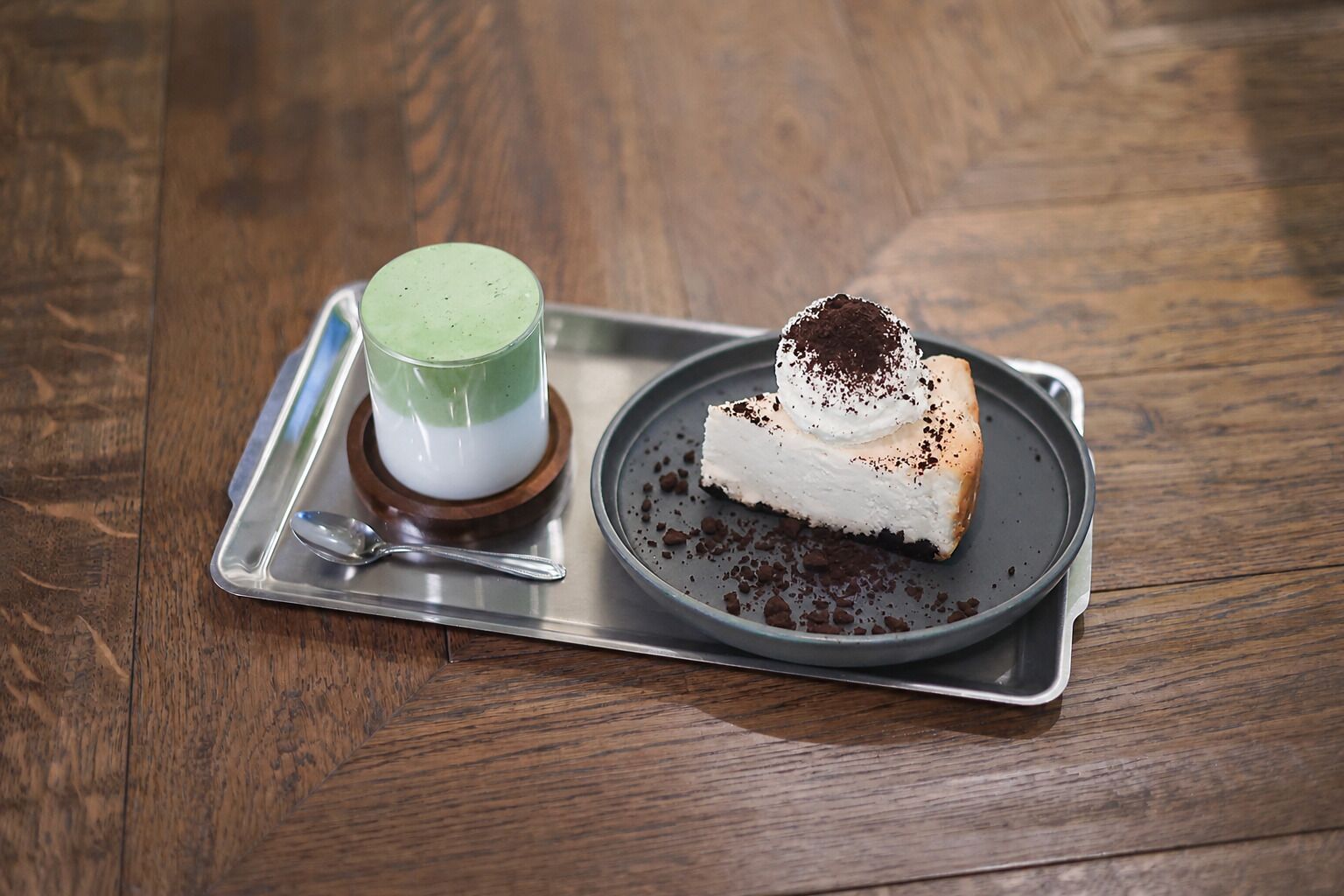 A dessert tray with a slice of cheesecake and a layered beverage on a wooden table.
