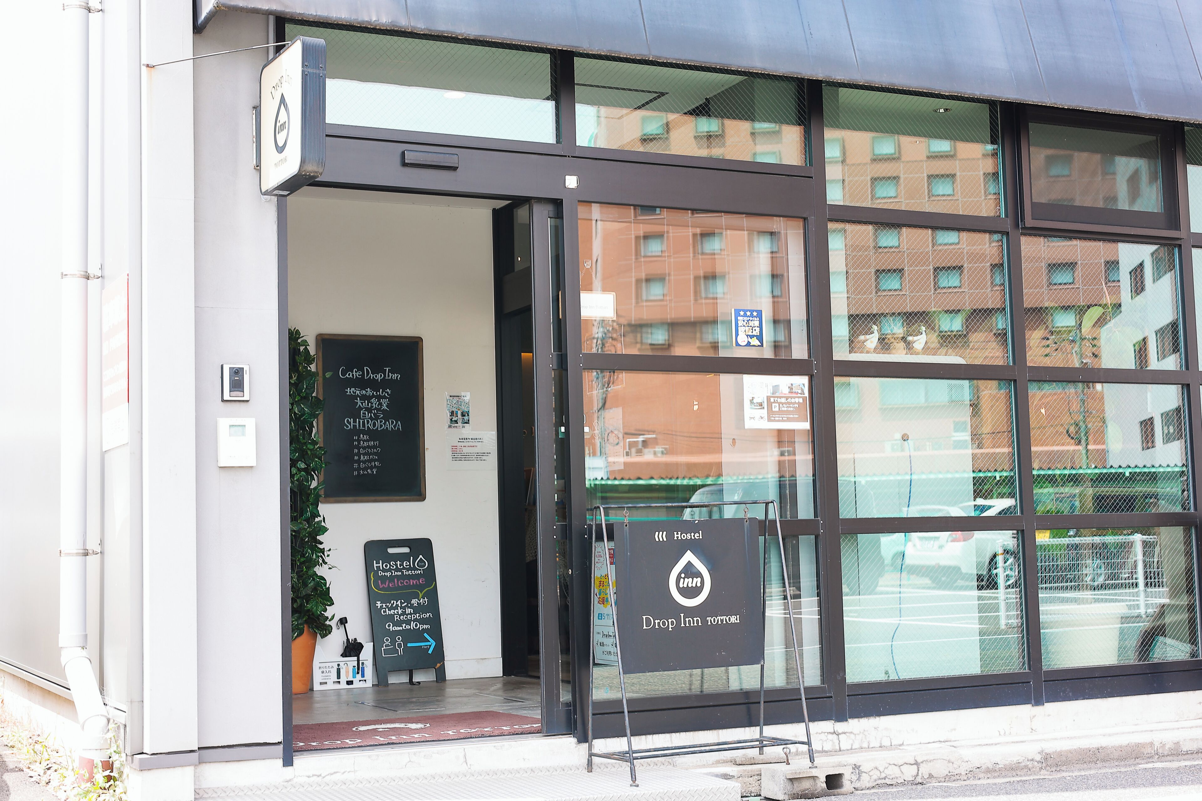 A hotel entrance with a reception desk, a sign indicating a hostel, and a view of the street and buildings in the background.