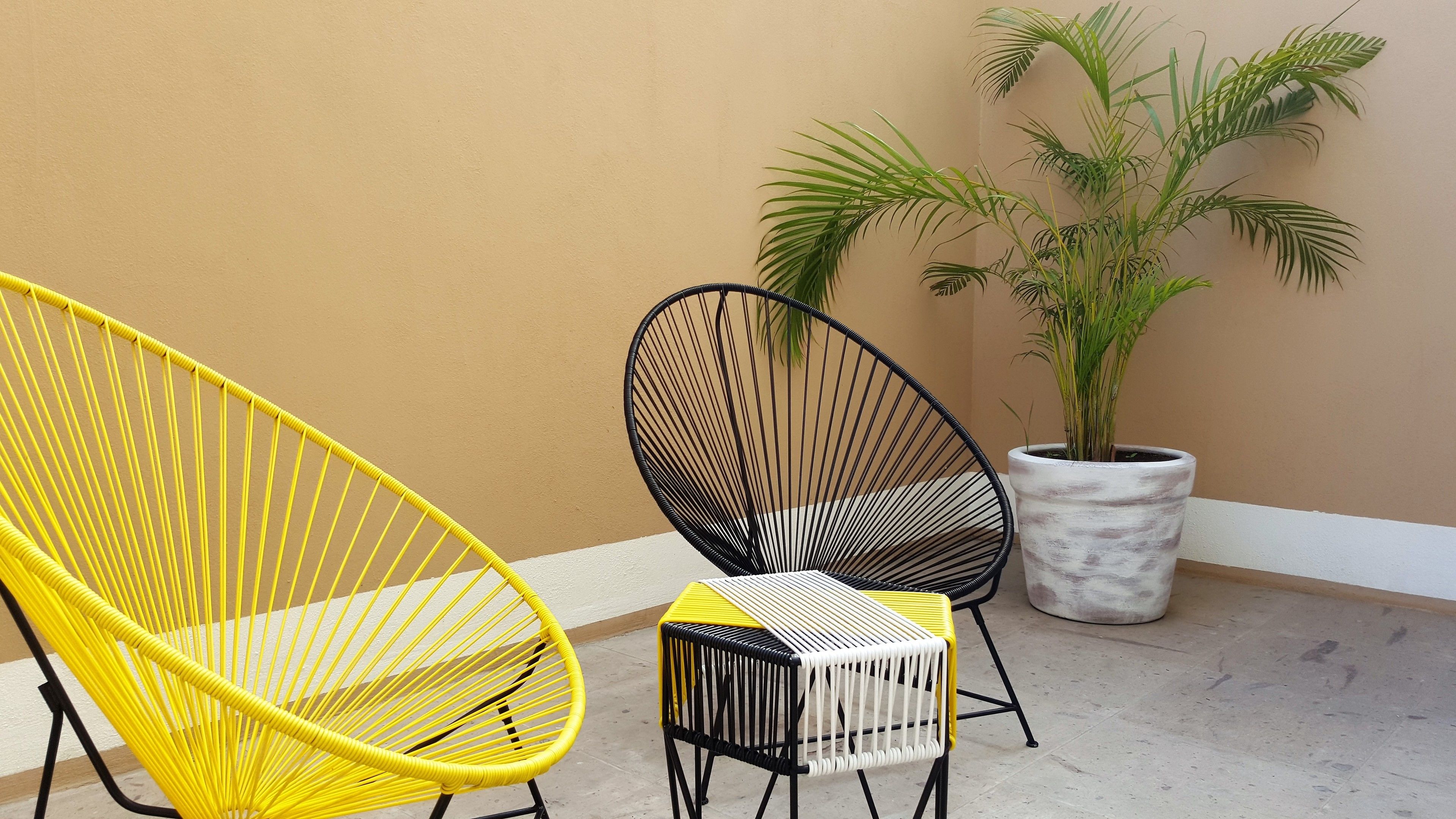 Deux fauteuils en osier avec des coussins jaunes et noirs, une plante en pot et un sol carrelé.