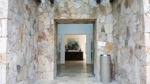 A stone-walled entrance to a building with a glass door, a painting on the wall, and a trash bin to the right. - Hotel Catedral (La Paz)