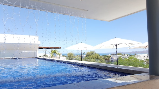 A swimming pool with water jets, a view of the sea, and umbrellas. - Hotel Catedral (La Paz)