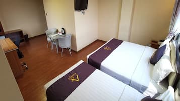A hotel room with two beds, a desk, a chair, and a TV on the wall.