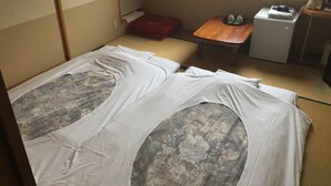Ein traditioneller japanischer Raum mit Tatami-Bodenbelag, einer Futon-Liege, einem kleinen Holztisch und einer kompakten Küchenzeile.