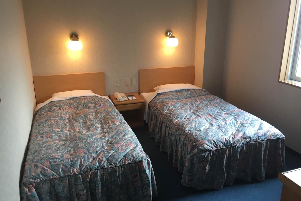 Une chambre d’hôtel avec deux lits simples, chacun recouvert d’une couvre-lit à motifs, une table de chevet avec un téléphone et des lampes fixées au mur.